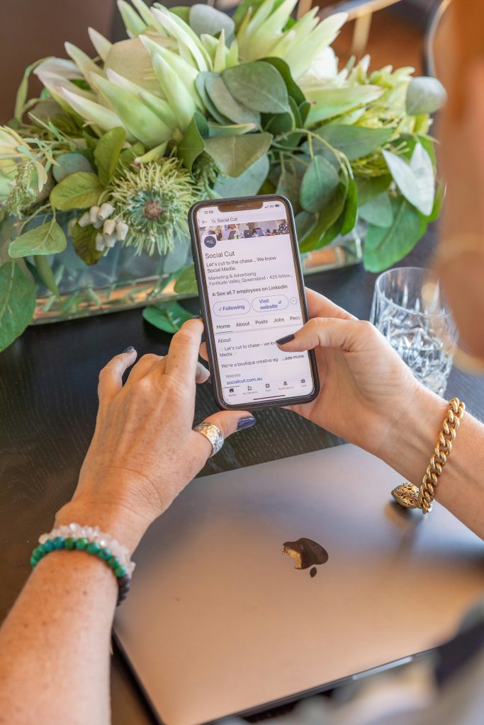 Person viewing a small business’s LinkedIn profile on their phone, highlighting how social platforms support visibility but don’t replace the control and credibility of having your own website.